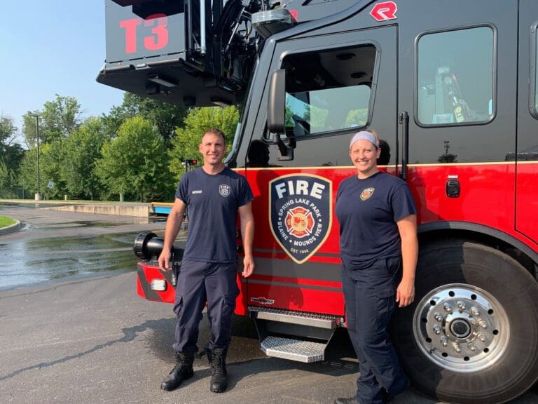 Two Fire Fighters Pose In Front Of Fire Truck